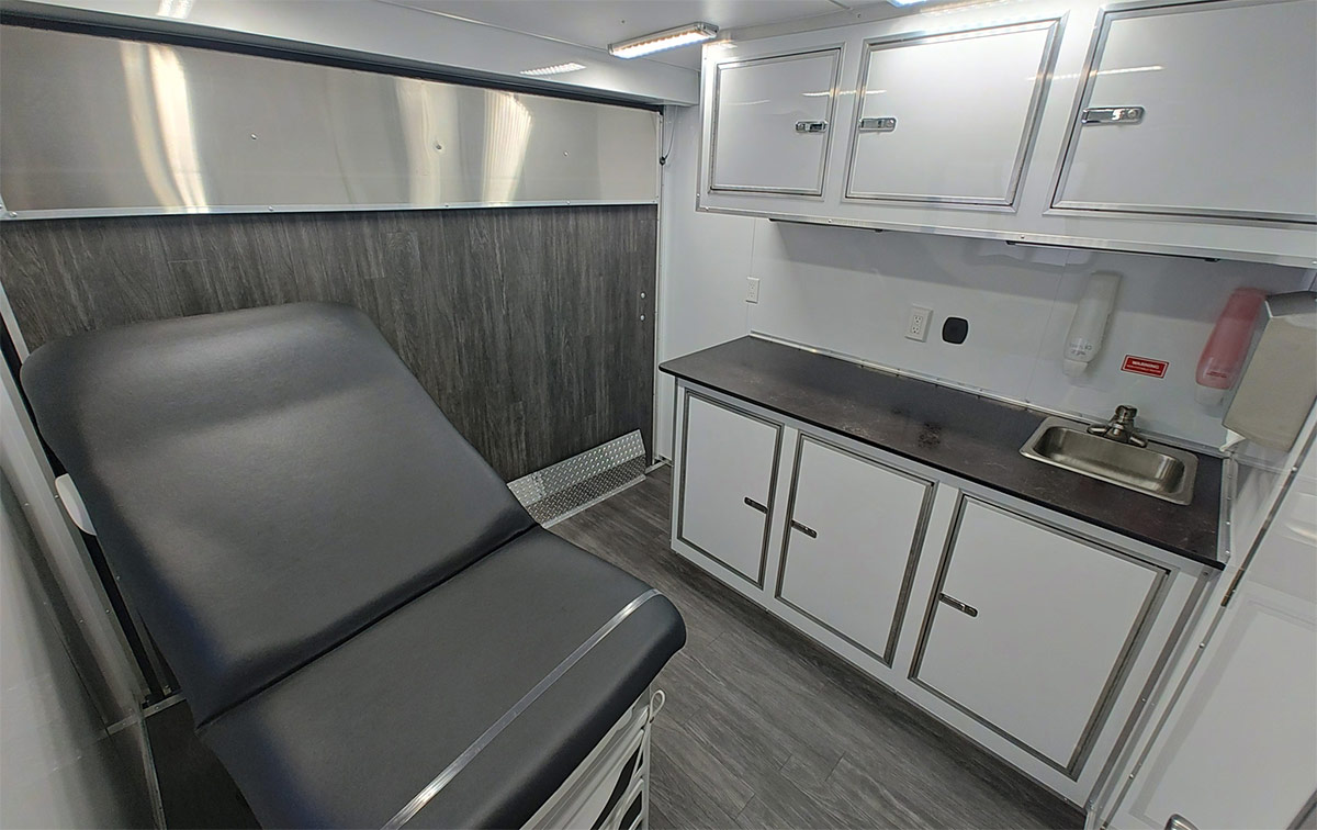 A patient bed next to a bare countertop and sink.